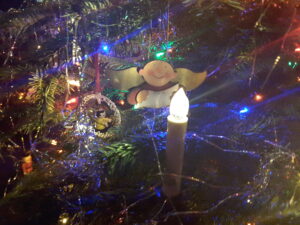Weihnachtsengel mit Gesangsblatt im Weihnachtsbaum hinter einer LED-Kerze