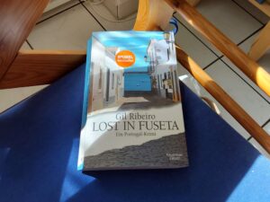 Das Cover der Taschenbuchausgabe von Gil Ribeiros "Lost in Fuseta" auf blauem, halb sonnigem, halb schattigem Grund.