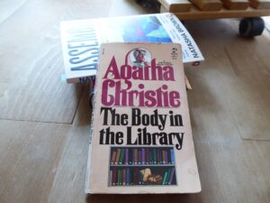 Ein Stapel Bücher auf dem Fußboden, obenauf eine Taschenbuchausgabe von Agatha Christies "The Body in the Library"
