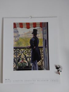 Kalenderblatt Mai 2024 mit einem Gemälde von Gustavev Caillebotte, dass einen Mann mit Zylinder in Rückenansicht auf dem Balkon einer Stadtwohnung zeigt