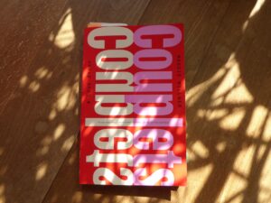 Das Cover von Maggie Millners Roman "Couplets" auf einem Holzfußboden im Halbschatten
