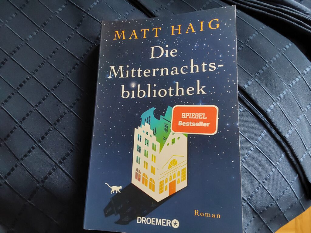 Das Cover von Matt Haigs "Die Mitternachtsbibliothek" auf einer dunkelblauen Tagesdecke