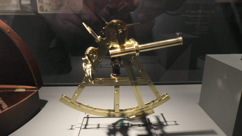 Ein blitzblanker Sextant aus Messing sticht vor dem dunklen Hintergrund in seinem Schaukasten hervot.