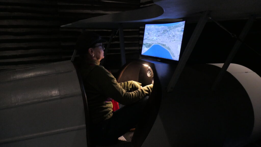 Die Autorin sitzt im Nachbau eines Wasserflugzeuges am Ruder, vor sich einen hellen Bildschirm, der den Wasserflughafen bei Tallinn von oben zeigt. Das Ganze ist ein Simulator und weil die Umgebung drumherum im Dunkel verschwindet, wirkt die Simulatorpilotin um so konzentrierter,