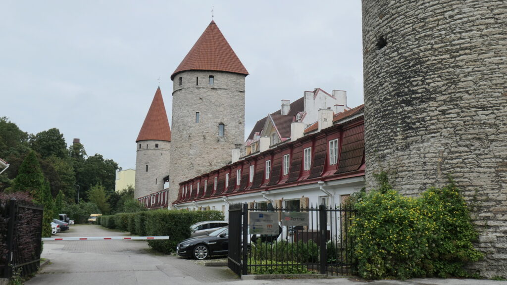 Mittelalter trifft modernes Wohnen: Blick die Stadtmauer entang Richtung Plate Tower. Auf der Parkseite der Mauer zieht sich eine Reihe schicker zweigeschossiger und dennoch niedrig wirkender Wohnhäuser mit Klappläden entlang. Stünden nicht große Luxuskarossen vor ihnen, könnte man irrtümlich annehmen, hinter der Schranke, die den Eintritt zu dieser Gasse verwehrt, lebten ganz normale Menschen ...