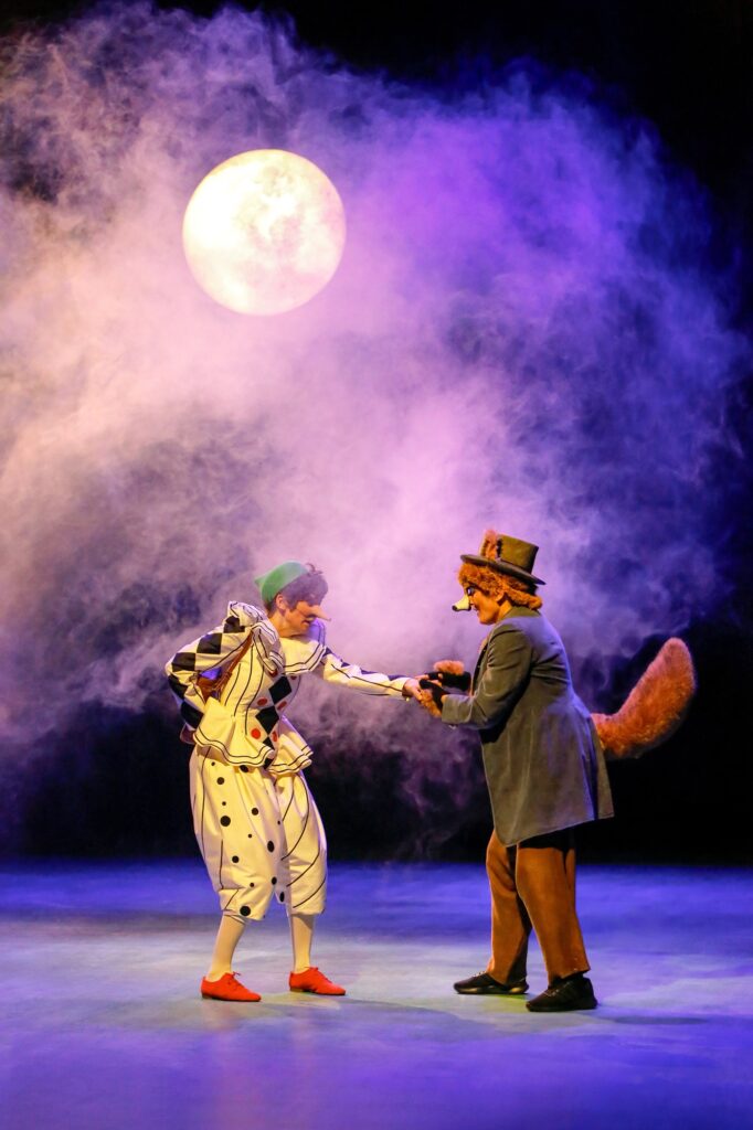 Unterm nebelumwaberten Vollmond ringen Pinocchio und der Fuchs um einen kleinen Beutl Gold.