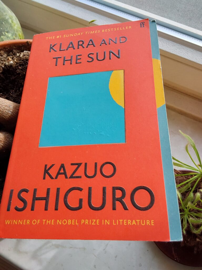 Das rote Cver von Kazuo Ishiguros "Klara and the Sn" hat in der Mitte ein hellblaues Rechteck, in dessen rechter oberer Ecke ein gelber Kreisausschnitt zu sehen ist - als luge die Sonne in ein Fenster hinein.